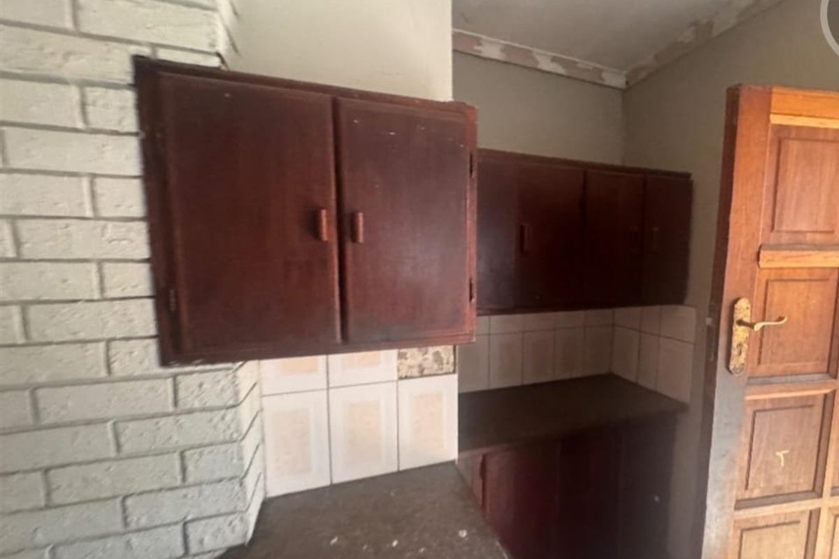 A dated kitchen area featuring built-in wooden cabinetry, stone countertops, and a brick feature wall, offering potential for a modern renovation.