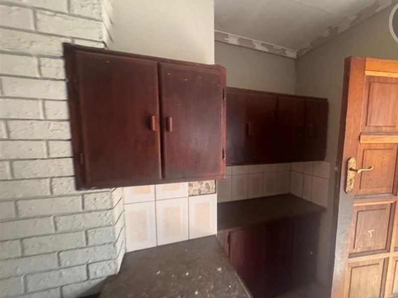 A dated kitchen area featuring built-in wooden cabinetry, stone countertops, and a brick feature wall, offering potential for a modern renovation.