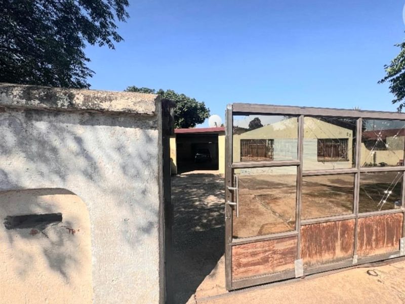 Front entrance view featuring a metal driveway gate, concrete boundary wall, and a carport leading to the main house structure.