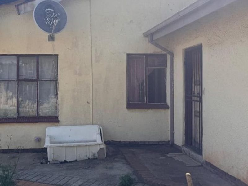 Rear exterior view of the property showing weathered walls, metal security gate, and paved walkway area.