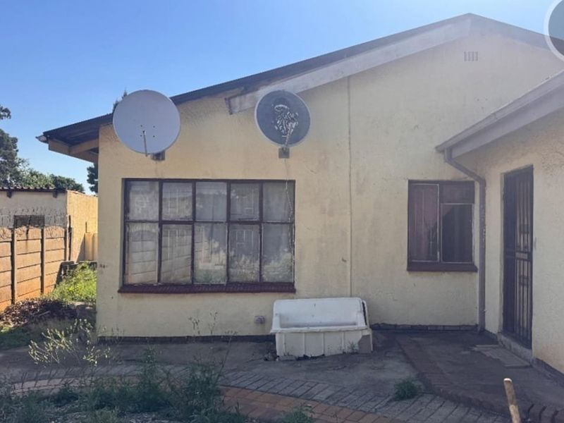 Rear exterior view of the house featuring a paved area, concrete wash trough, and metal window frames with visible signs of weathering and exterior wear.