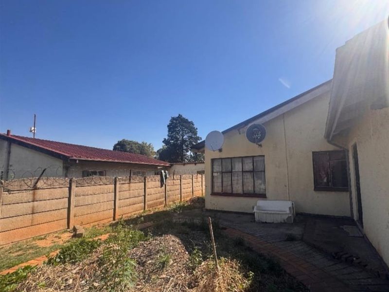 Rear view of the property featuring a paved walkway, precast boundary wall with security fencing, and an unmaintained garden area.