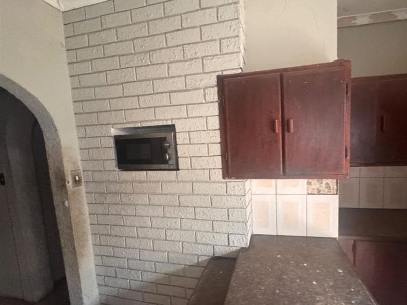 A dated kitchen area featuring a brick feature wall with a built-in microwave, dark wooden cabinetry, and a tiled backsplash requiring renovation.