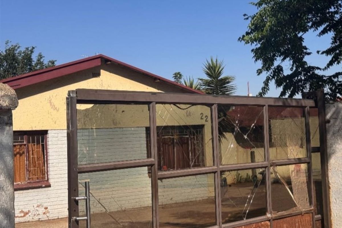 Front exterior view of a residential property featuring a metal security gate and brick facade with visible signs of wear and maintenance requirements.