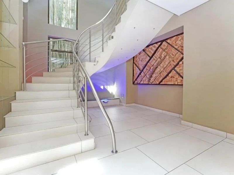 A bright and modern entrance hall featuring a striking curved staircase with stainless steel balustrades and elegant tiled flooring.