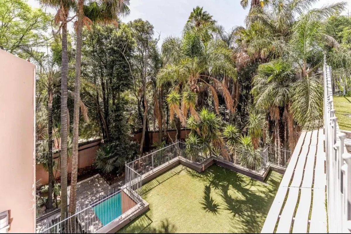 Elevated view of a rear garden featuring a small swimming pool, artificial lawn, and mature trees enclosed by a metal balustrade.