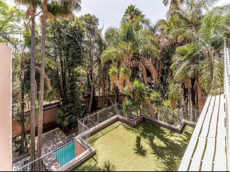 Elevated view of a rear garden featuring a small swimming pool, artificial lawn, and mature trees enclosed by a metal balustrade.