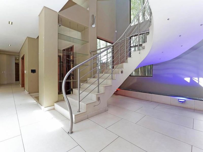 Spacious entrance hall featuring a striking curved staircase with stainless steel balustrade, modern tiled flooring, and integrated accent lighting.