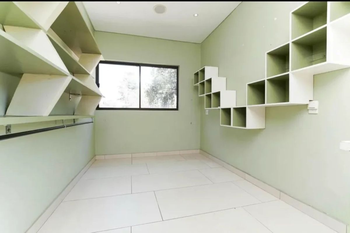 An empty bedroom featuring light green walls, tiled flooring, and extensive built-in wall shelving units.