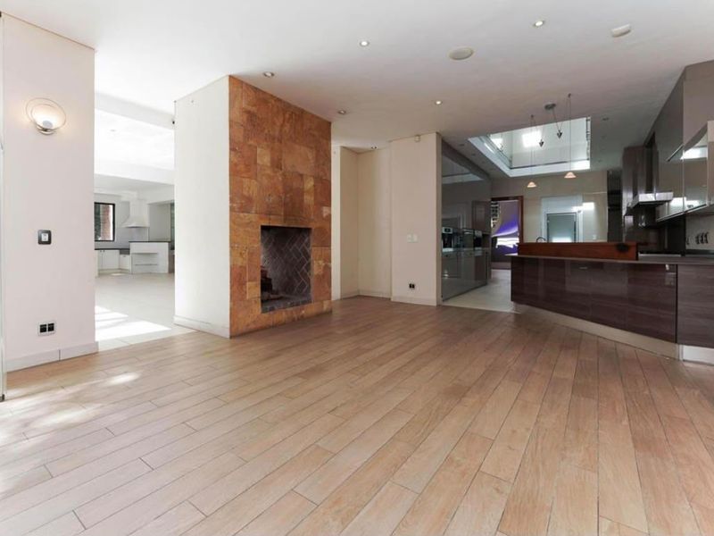 Spacious open-plan living area featuring a striking stone-clad fireplace, modern kitchen with integrated appliances, and abundant natural light from a central skylight.