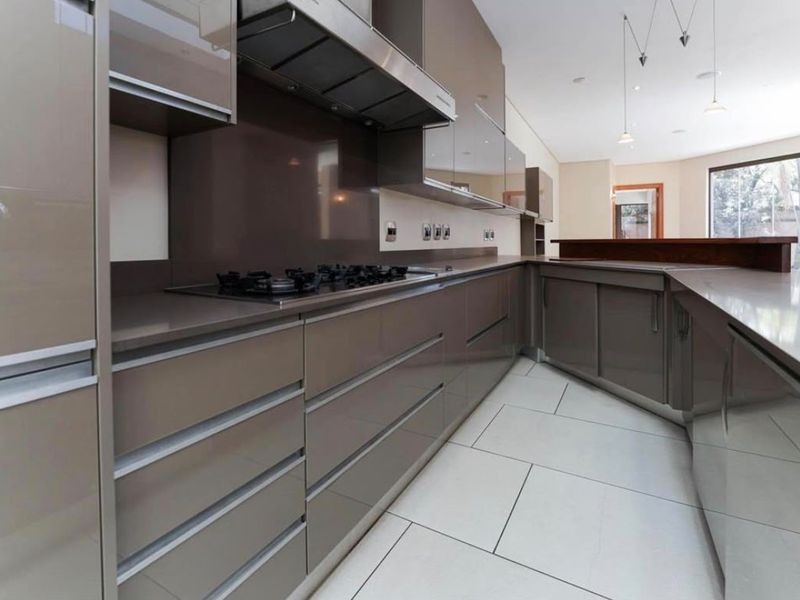 Modern kitchen featuring sleek high-gloss cabinetry, stone countertops, a gas hob with extractor, and large format floor tiles.