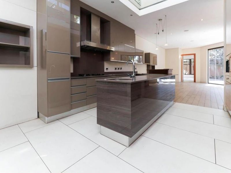 Modern kitchen featuring a central island, high-gloss cabinetry, built-in appliances, and sleek tiled flooring in an open-plan layout.