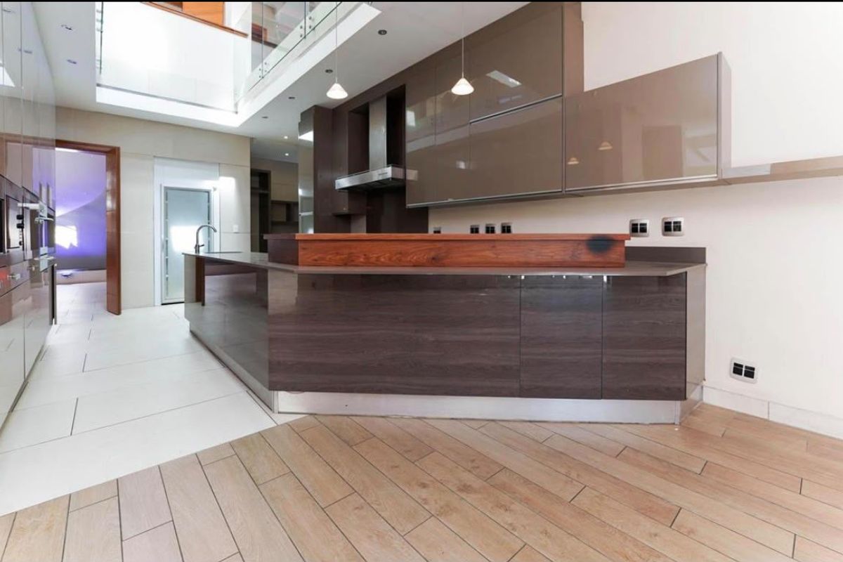 Modern kitchen featuring high-gloss cabinetry, a large central island with a wooden breakfast bar, and a seamless blend of tiled and wood-look flooring.