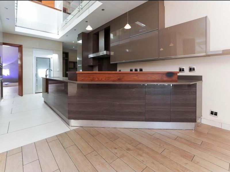 Modern kitchen featuring high-gloss cabinetry, a large central island with a wooden breakfast bar, and a seamless blend of tiled and wood-look flooring.