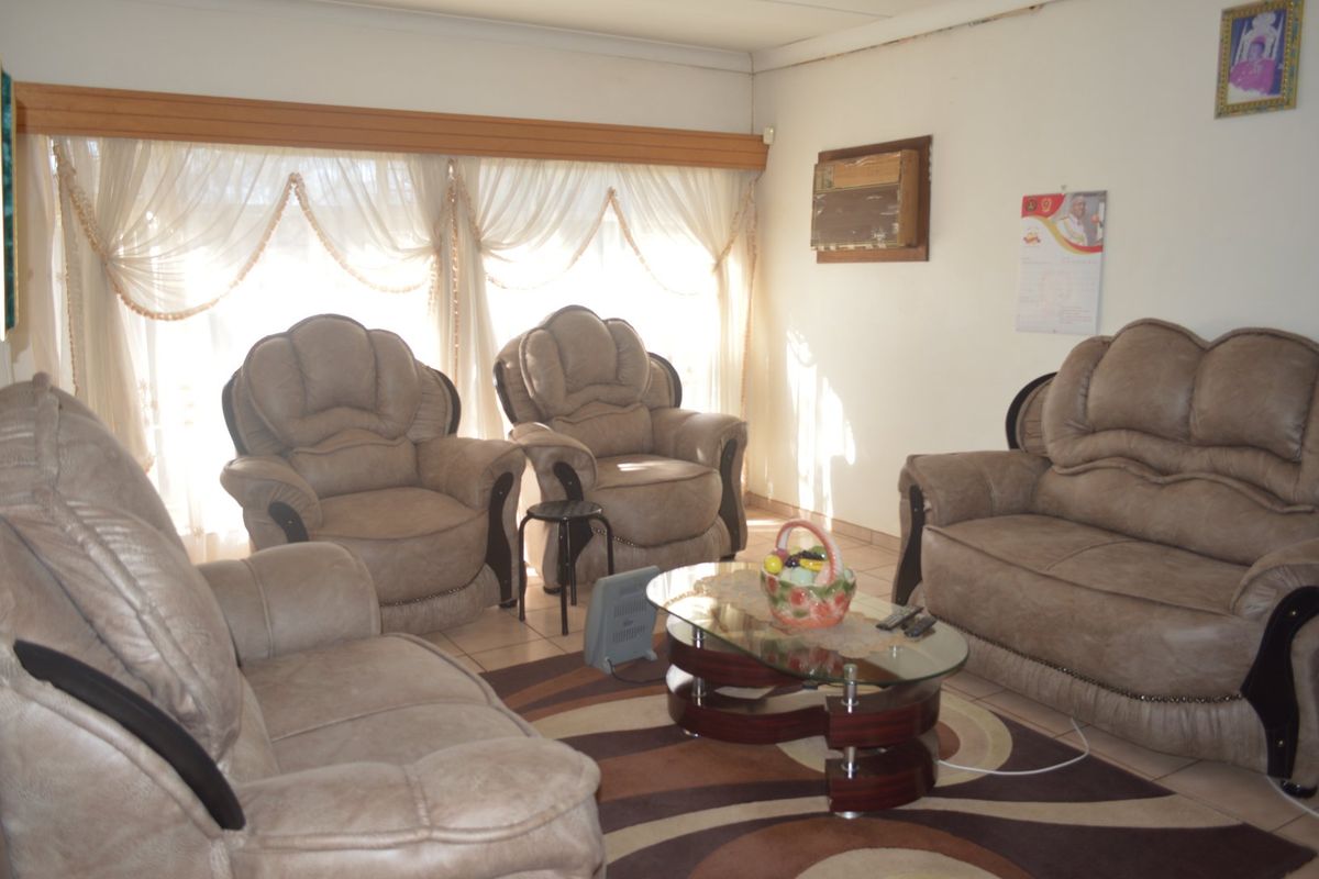A living room featuring tiled flooring and a wall-mounted air conditioning unit, with natural light entering through large windows.