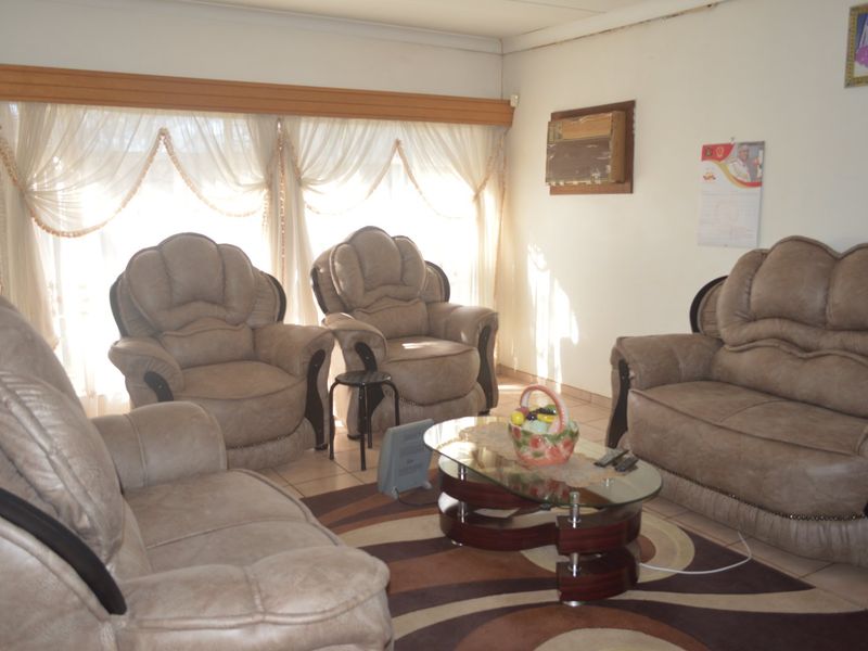 A living room featuring tiled flooring and a wall-mounted air conditioning unit, with natural light entering through large windows.