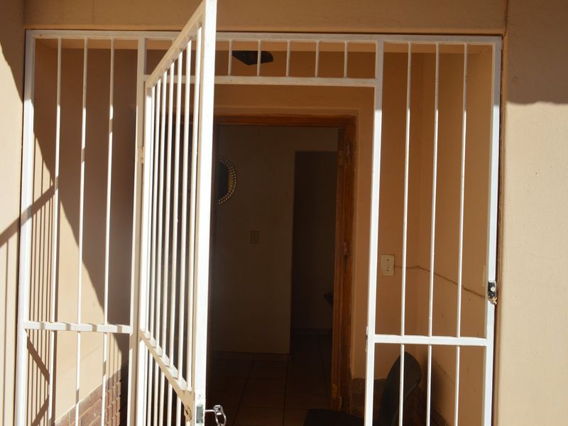 Entrance area featuring a white security gate and tiled flooring, showing signs of wear and wall cracking.