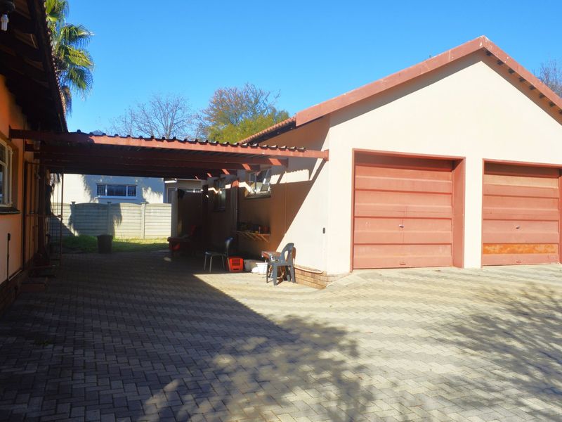 Rear exterior view featuring a double garage with a paved driveway and an attached carport structure.