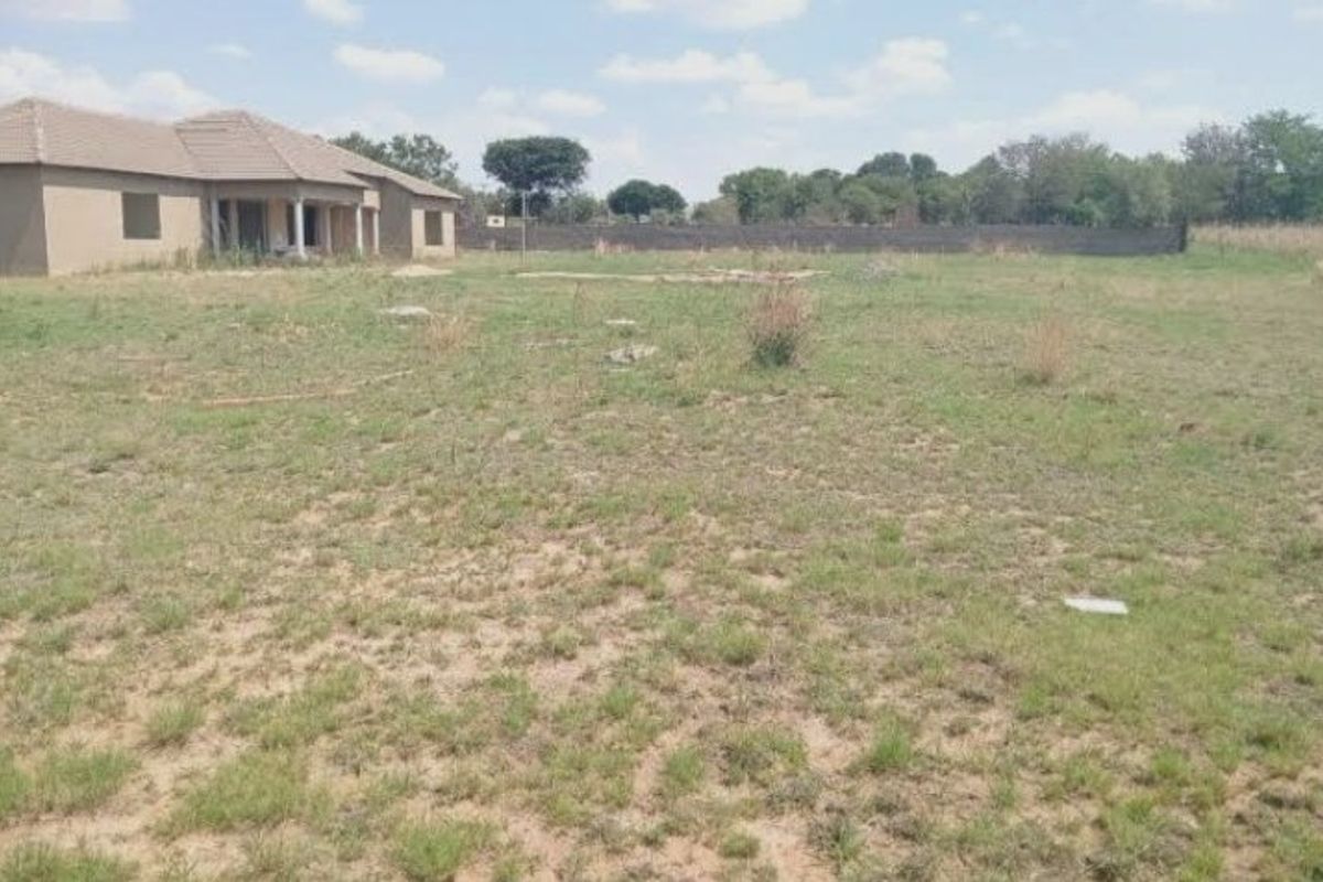 A wide view of the rear yard showing the back elevation of the house with a covered patio and surrounding perimeter wall.