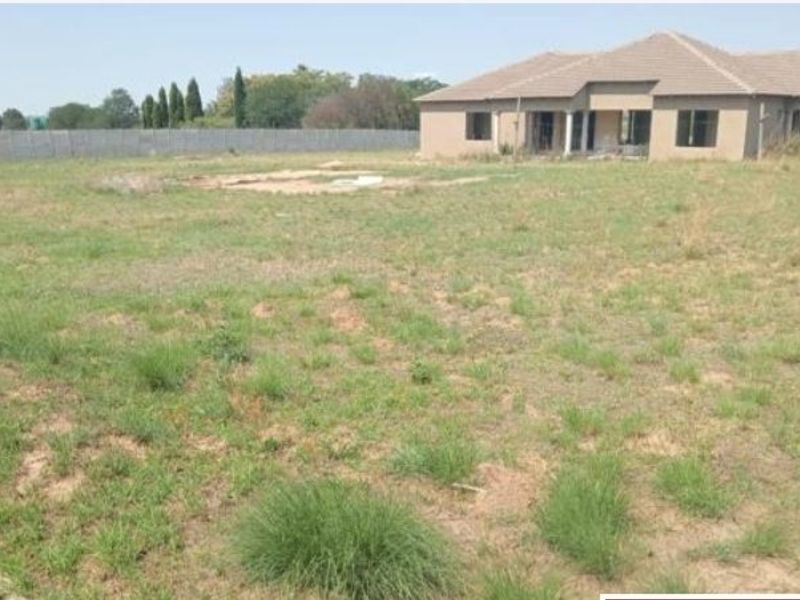 A view of the rear elevation of a farm property featuring a large undeveloped garden area and a single-story dwelling with a tiled roof.