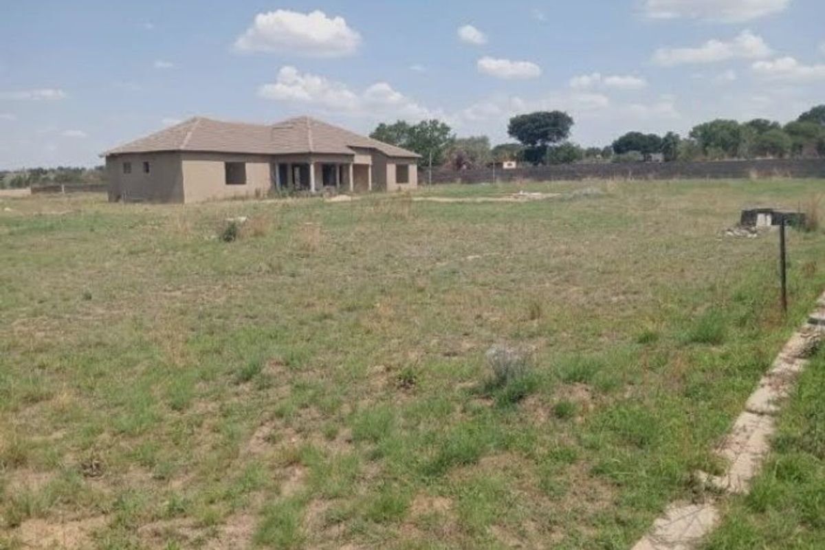 A view of a large, unfinished residential property on a spacious plot of land, featuring a tiled roof structure and surrounding perimeter wall.
