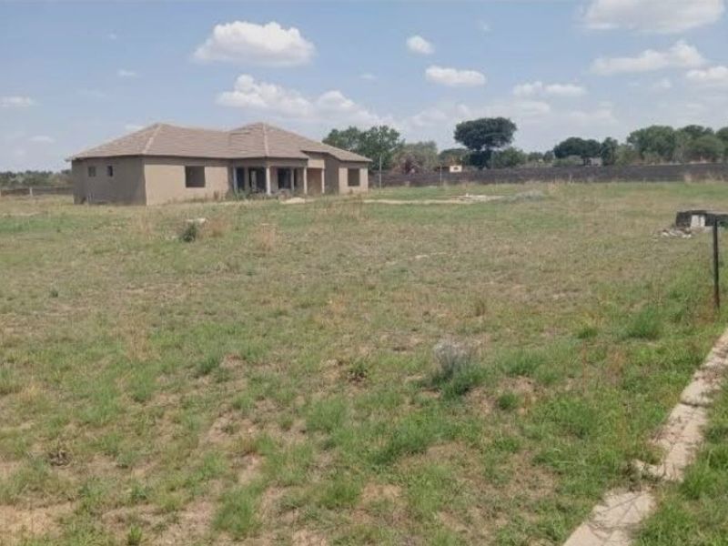 A view of a large, unfinished residential property on a spacious plot of land, featuring a tiled roof structure and surrounding perimeter wall.