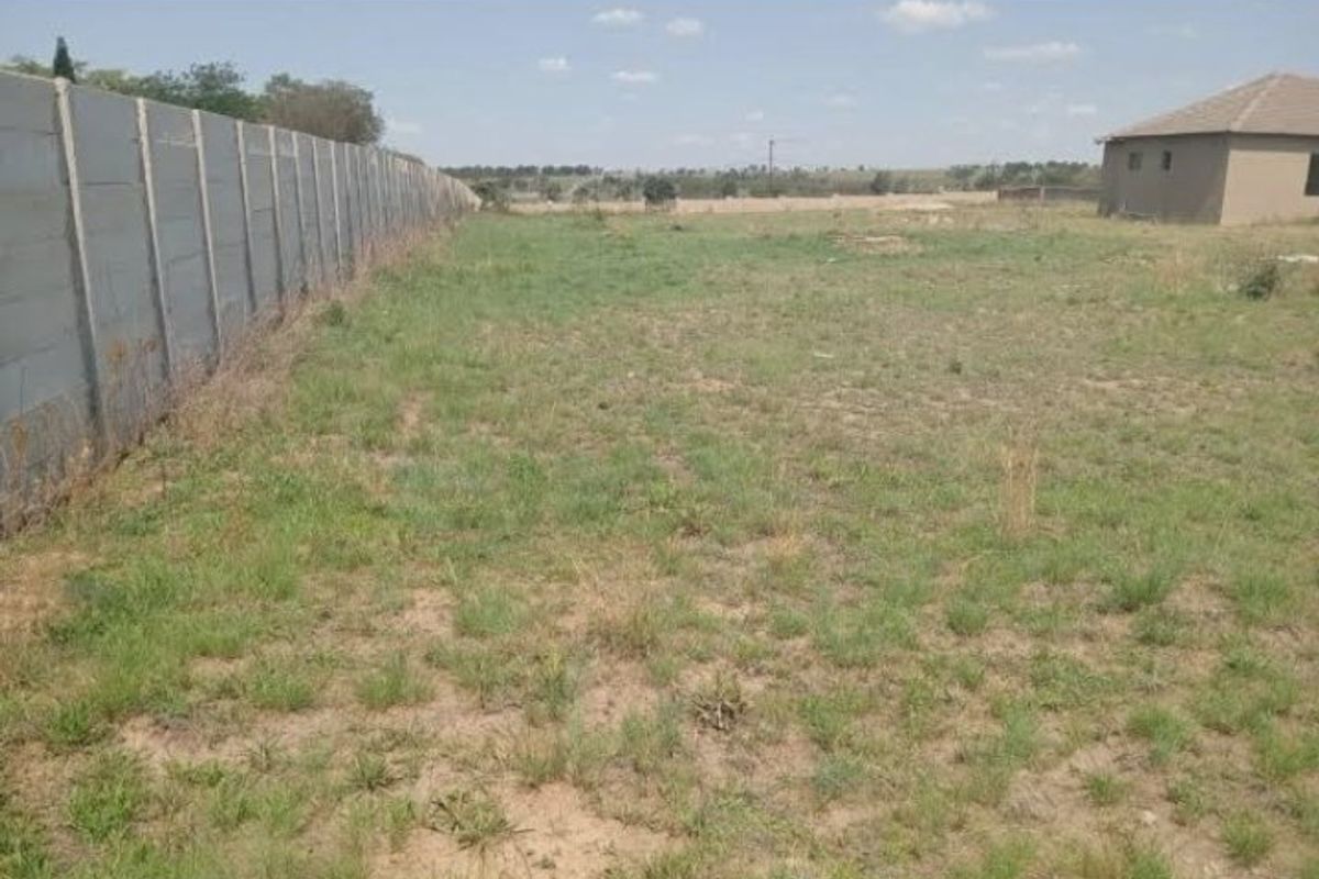 A vacant residential plot featuring a long precast concrete boundary wall and open grassed area.