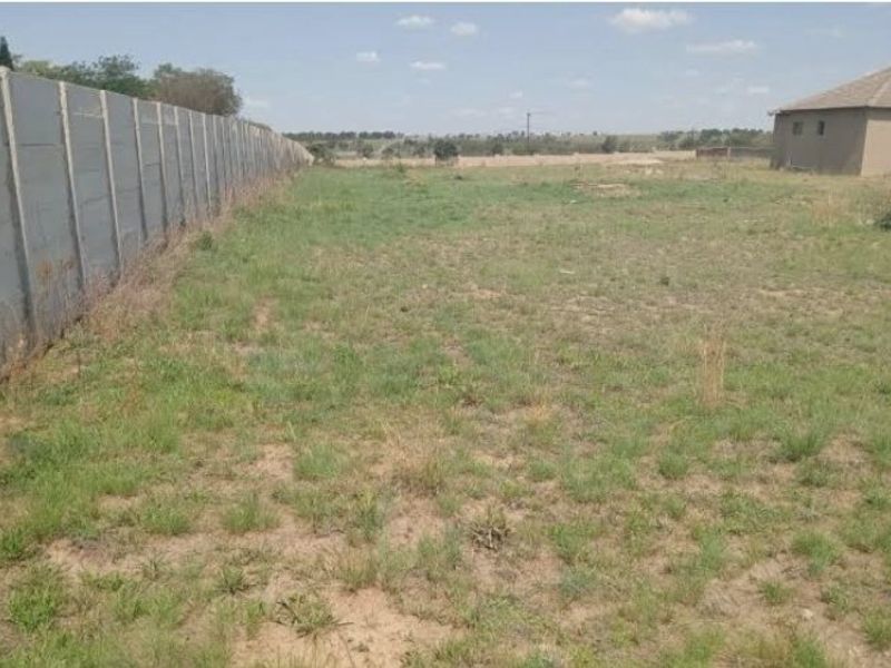 A vacant residential plot featuring a long precast concrete boundary wall and open grassed area.