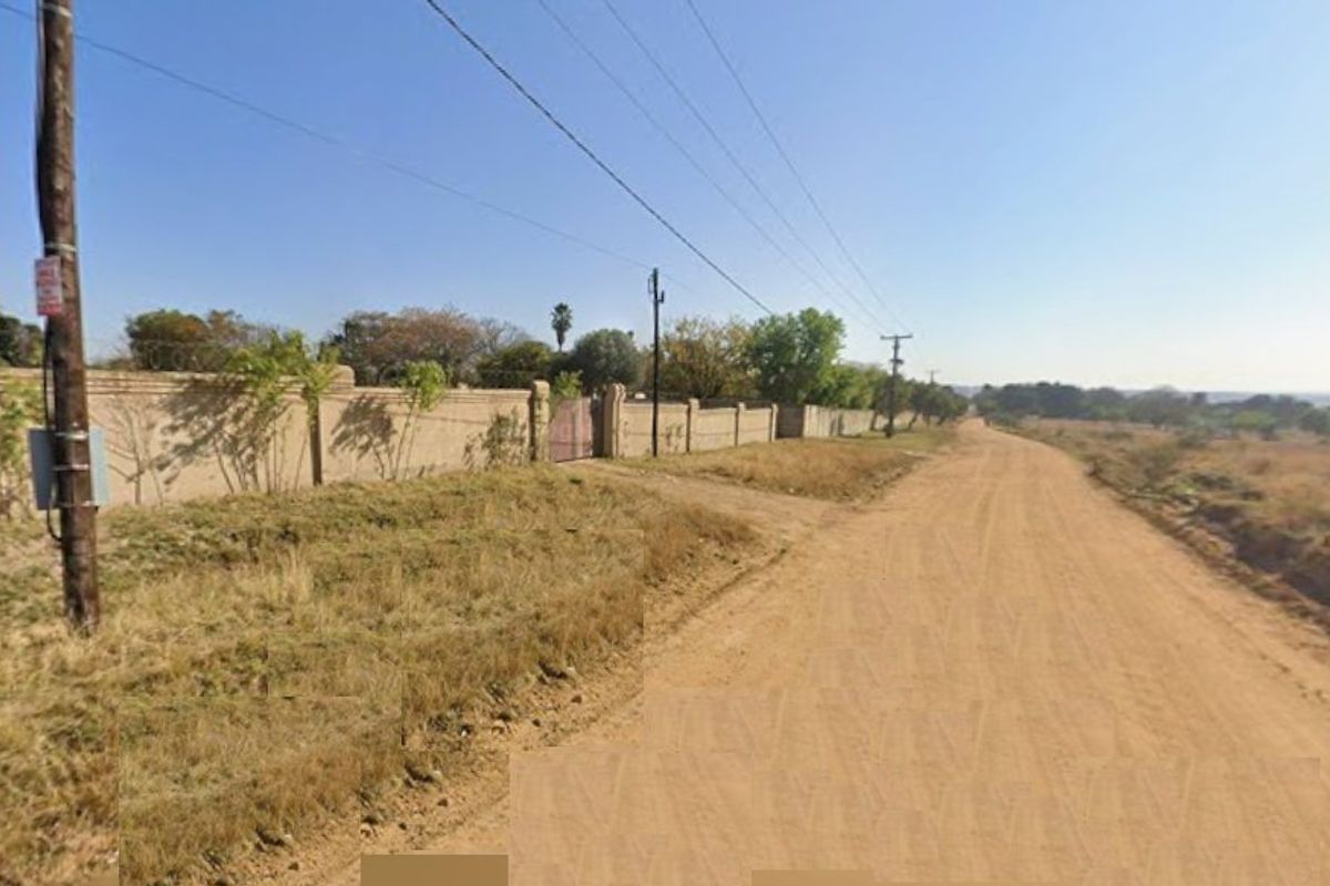 A view of an unpaved road leading to a property enclosed by a perimeter wall and gate.