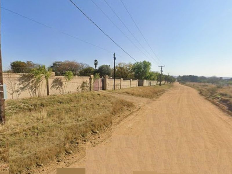 A view of an unpaved road leading to a property enclosed by a perimeter wall and gate.