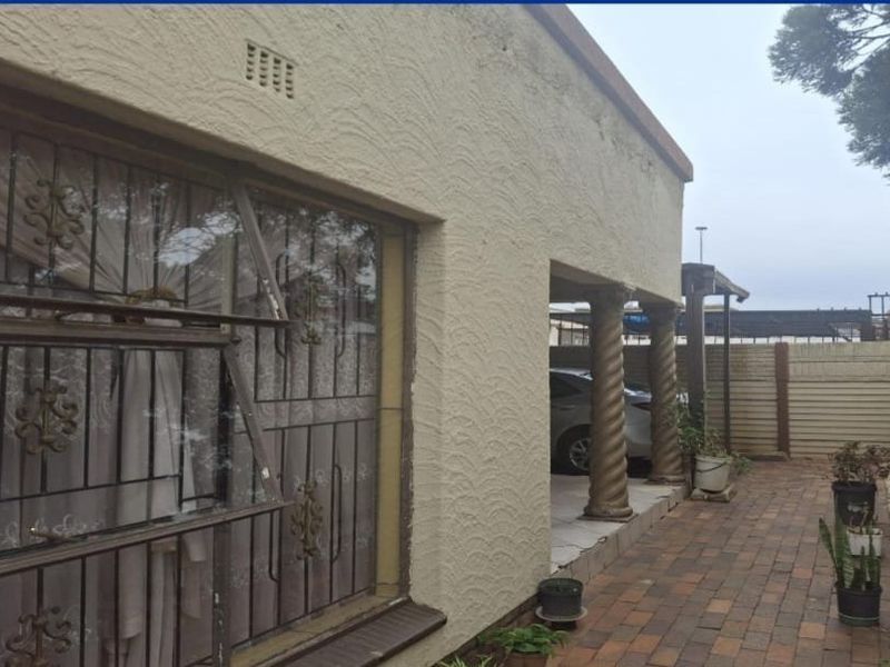 Rear exterior view featuring a textured facade, decorative columns, paved patio area, and secure window bars.