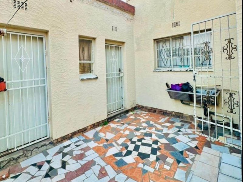 A rear courtyard area featuring a mosaic-tiled patio, security gates, and a wall-mounted utility sink, offering potential for outdoor renovation.