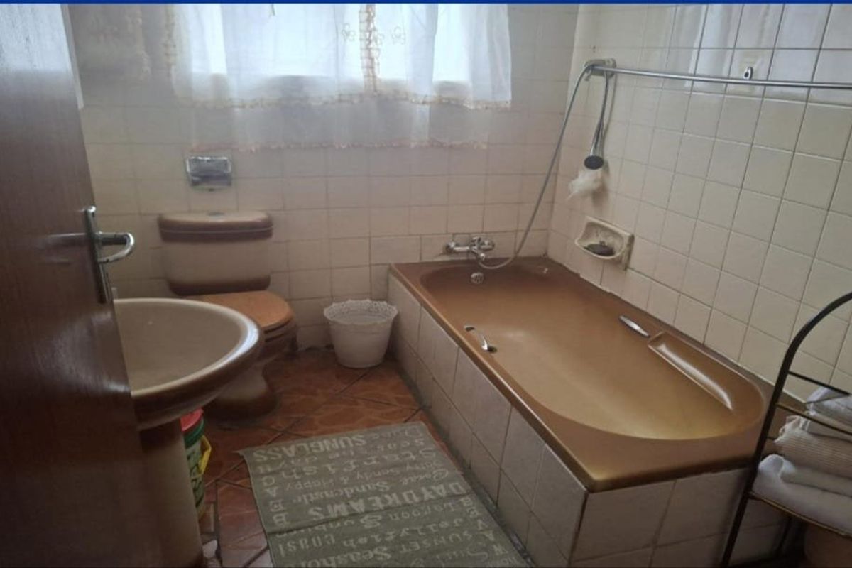 A dated bathroom featuring a brown bathtub, matching toilet, pedestal basin, and tiled finishes throughout.