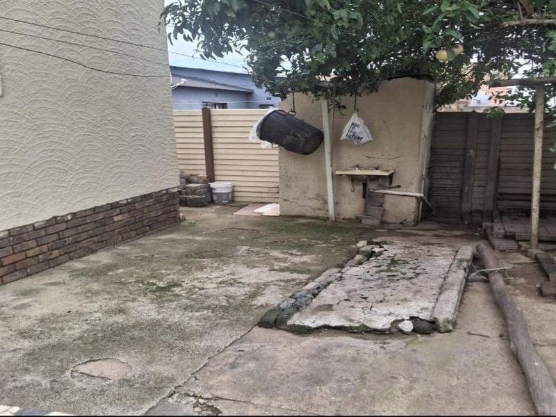 Rear exterior area featuring concrete paving, perimeter walling, and an external wash basin, requiring maintenance and landscaping to improve the outdoor space.