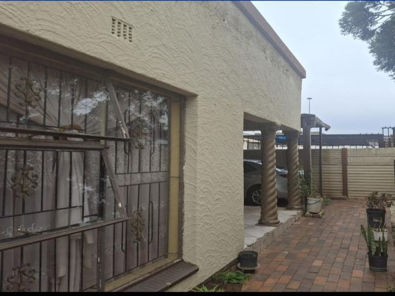 Front exterior view of the house featuring a textured facade, decorative columns, security bars on windows, and a paved driveway area.
