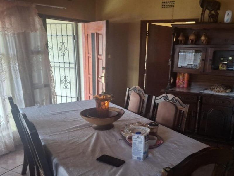 A dining room area featuring tiled flooring, a timber entrance door with a security gate, and a ceiling ventilation vent.