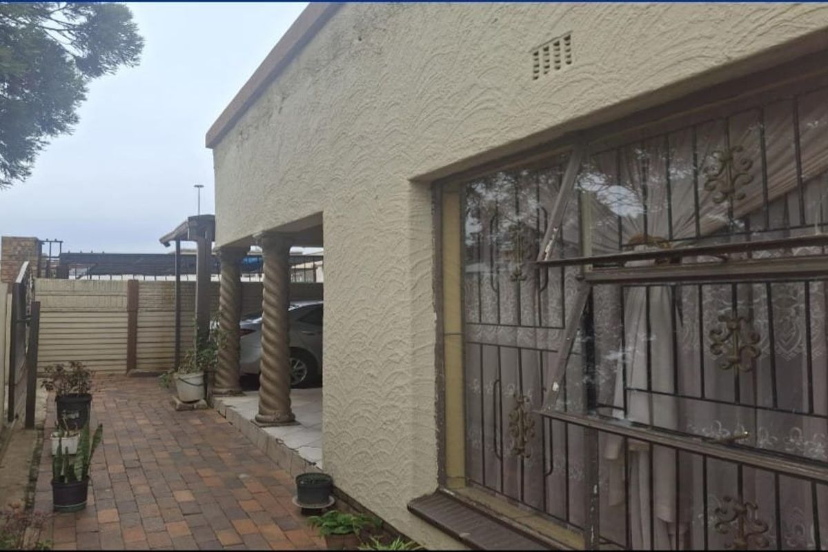 Rear exterior view of the house featuring a paved patio area, decorative columns, and windows fitted with security bars.