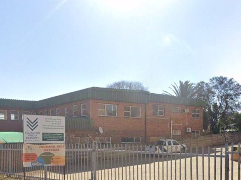 Front exterior view of a commercial brick building featuring a paved driveway, secure metal fencing, and external air conditioning units.
