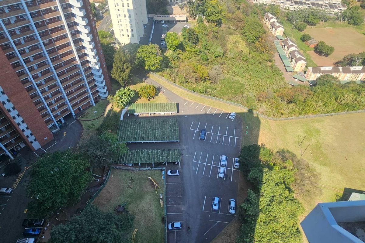 An aerial view of the apartment complex grounds, featuring paved parking bays, covered carports, and surrounding landscaped areas.