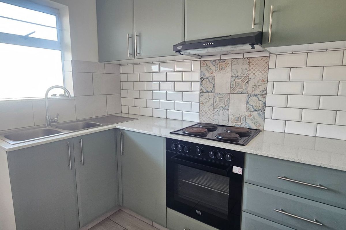 Modern kitchen featuring sage green cabinetry, stone countertops, subway tile backsplash with decorative accents, and integrated electric oven and hob.
