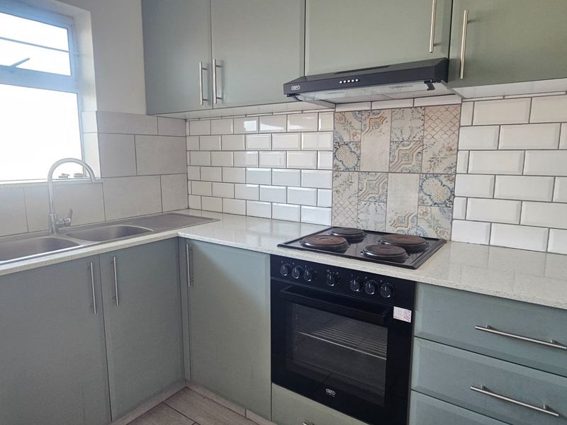 Modern kitchen featuring sage green cabinetry, stone countertops, subway tile backsplash with decorative accents, and integrated electric oven and hob.