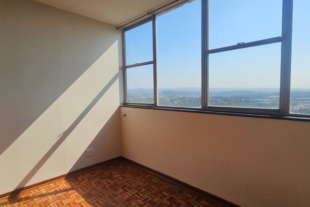 An empty bedroom featuring classic parquet flooring and expansive windows offering panoramic views, providing a bright and versatile space for customization.