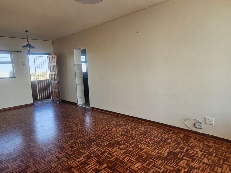 An empty living room featuring classic parquet flooring, a security gate leading to an outdoor area, and built-in storage.