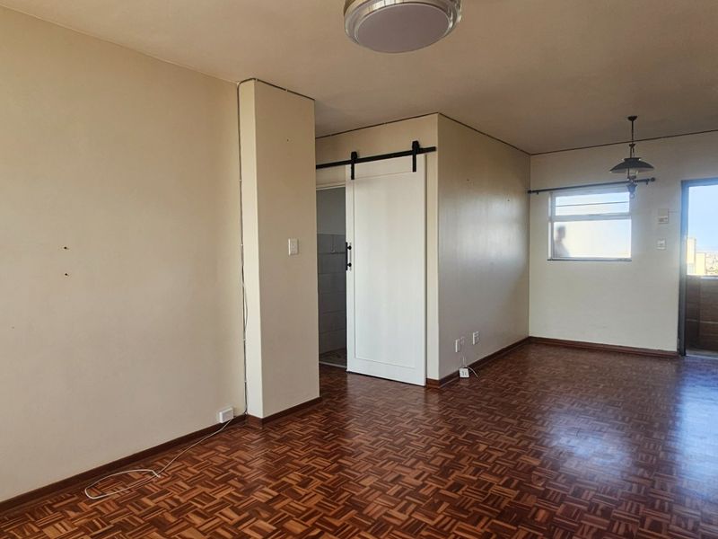 An empty living area featuring traditional parquet flooring, a sliding barn door, and access to an outdoor balcony through a security gate.