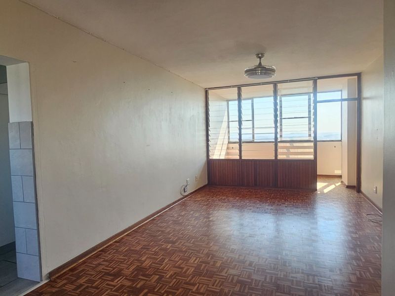 Spacious open-plan living area featuring classic parquet flooring, a ceiling fan, and large louvered windows, with an adjacent kitchen visible.