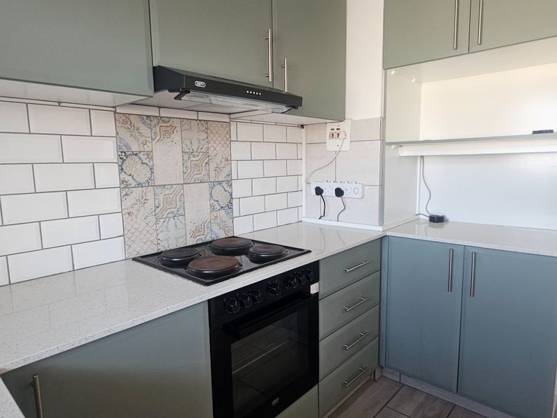 Modern kitchen featuring sage green cabinetry, stone countertops, subway tile backsplash, and integrated electric cooking appliances.