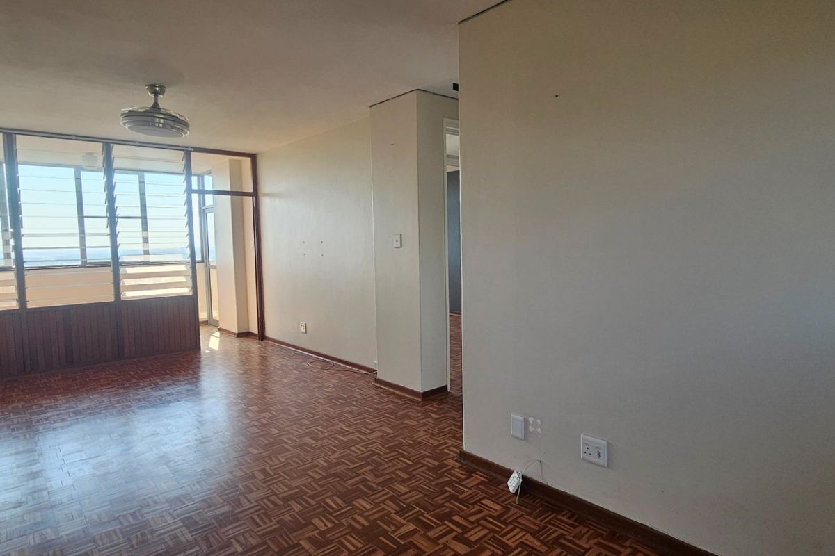 An empty living area featuring original parquet flooring, a ceiling fan, and large louvre windows that provide natural light and ventilation.