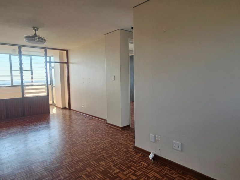 An empty living area featuring original parquet flooring, a ceiling fan, and large louvre windows that provide natural light and ventilation.