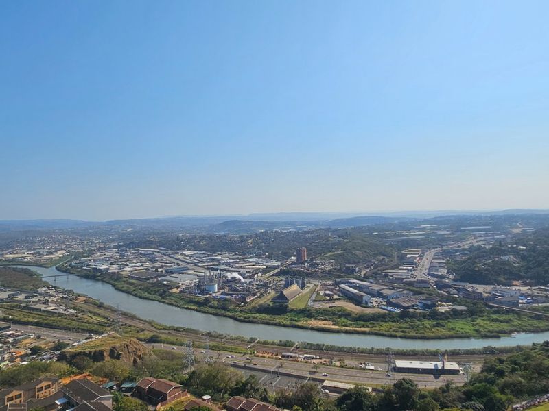 An elevated panoramic view overlooking a river, industrial area, and surrounding landscape.