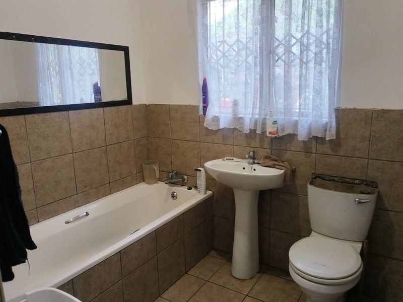 A functional bathroom featuring a bathtub, pedestal basin, and toilet with tiled finishes. The space requires minor repairs to the toilet cistern.